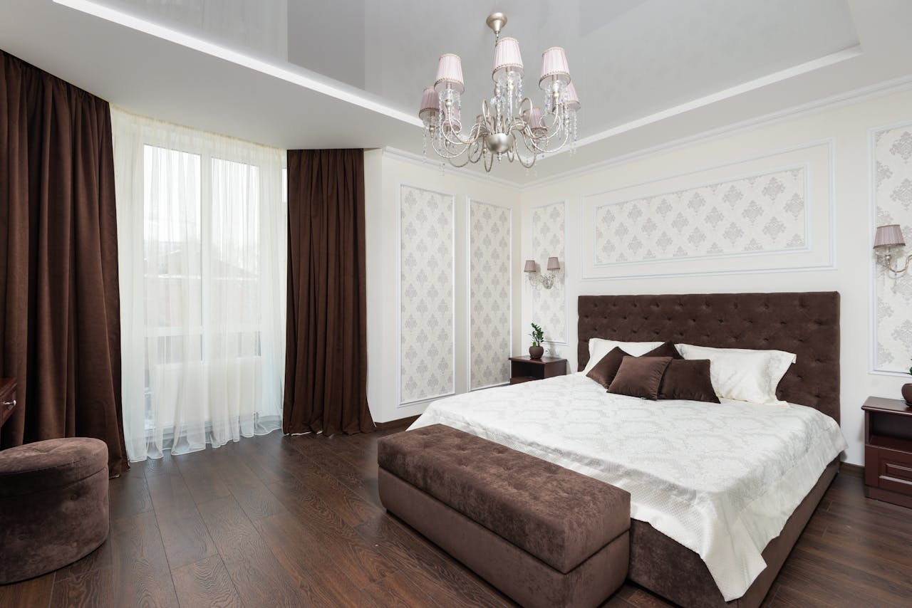 A contemporary bedroom featuring a luxury chandelier, brown accents, and a plush bed for a cozy atmosphere.